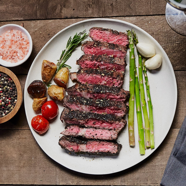 Medium rare boneless ribeye, cut and displayed with asparagus, potato, cherry tomato, garlic, and rosemary