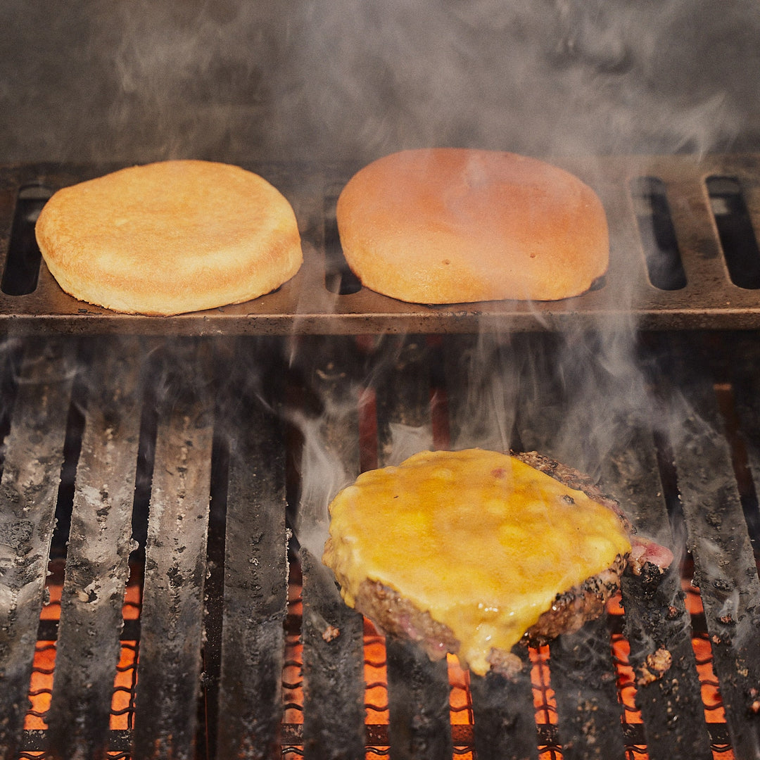 Cheese melting on a steak burger while buns toast behind