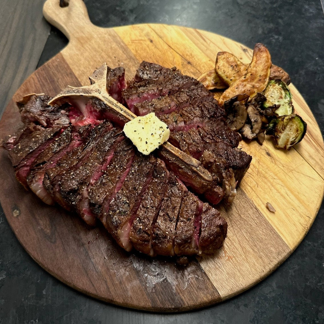 USDA Prime Porterhouse cut open to see medium rare inside with butter on top and Brussels sprouts and potatoes on the side