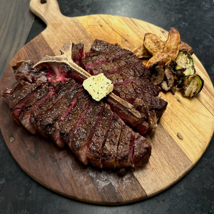 Juicy marbled porterhouse cooked medium rare with butter on top, potatoes and Brussels sprouts on the side