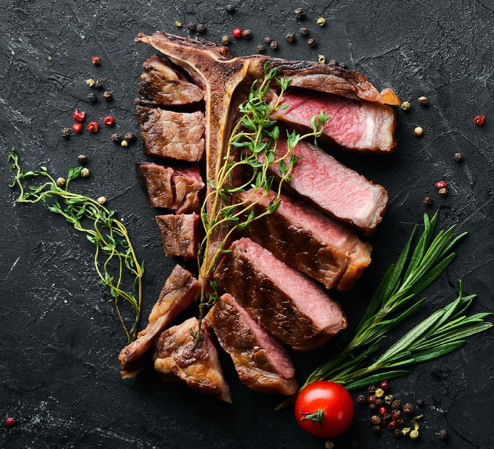 T-bone steak cooked medium-rare, cut and plated with thyme, rosemary, cherry tomatoes, and peppercorn