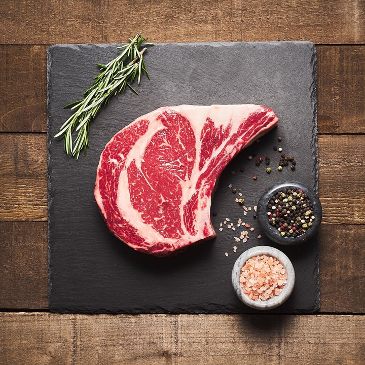 Wonderfully marbled Bone-in ribeye with salt, pepper and rosemary on the side