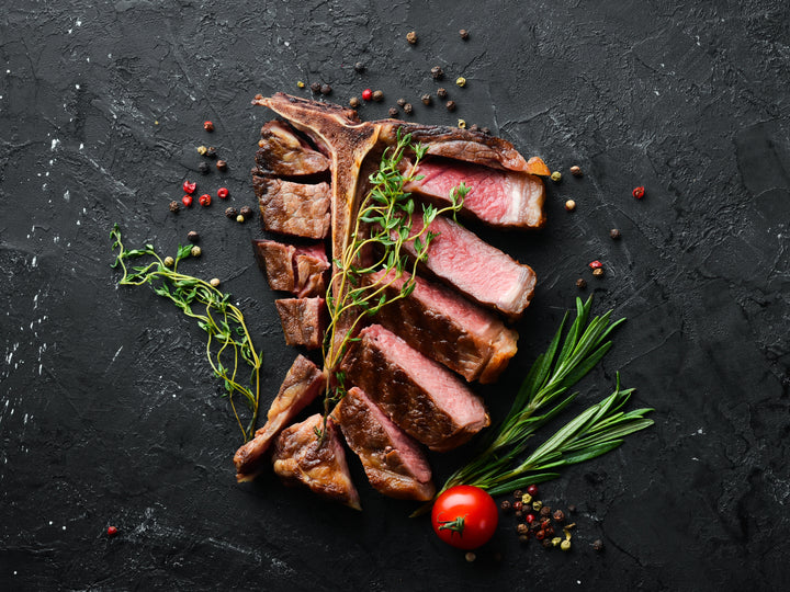 Perfectly cooked T-Bone with rosemary and thyme on the side, sliced to show colour of medium rare