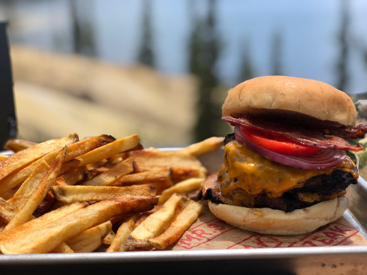 Juicy cheeseburger with bacon, tomato, and onions beside a side of fries