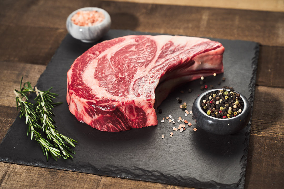 Thick cut of marbled Bone-in ribeye with side of salt, pepper, and rosemary