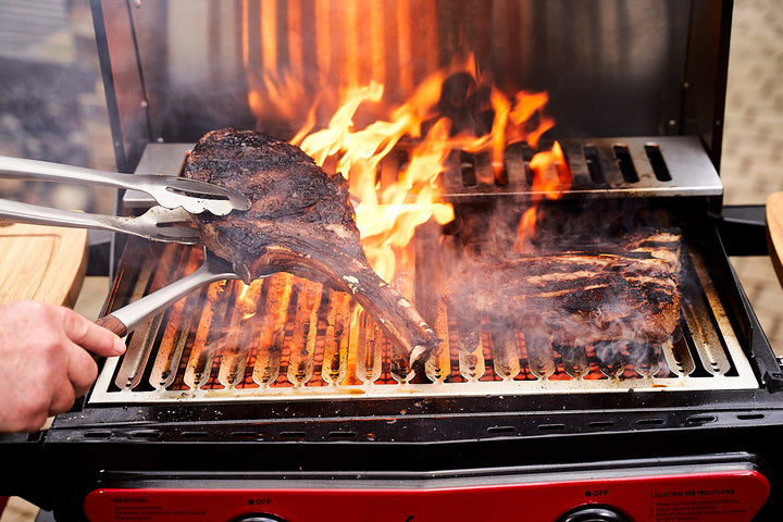 Tomahawk being flipped on a flaming grill